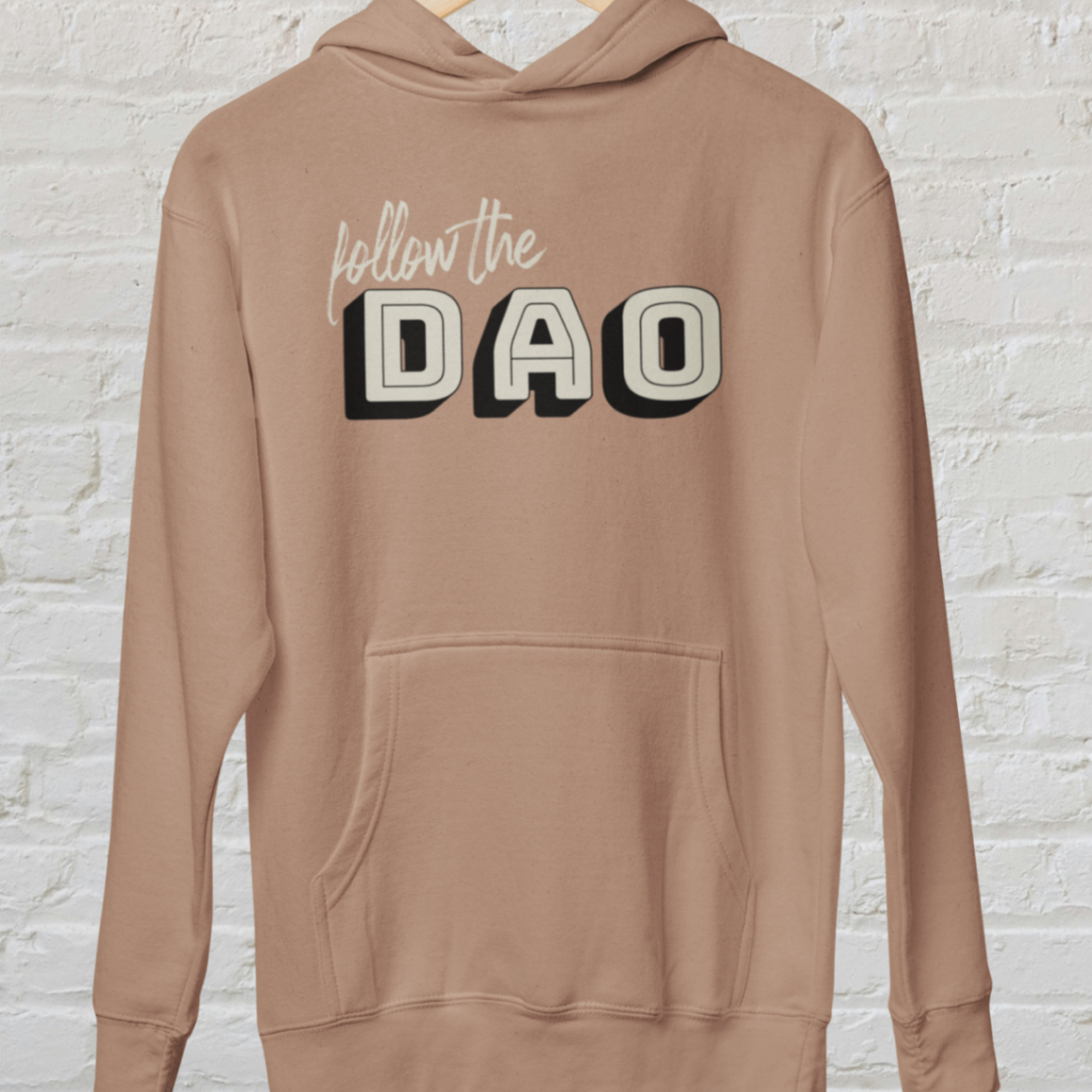 a caramel latte hoodie with follow the dao design over a white brick backround