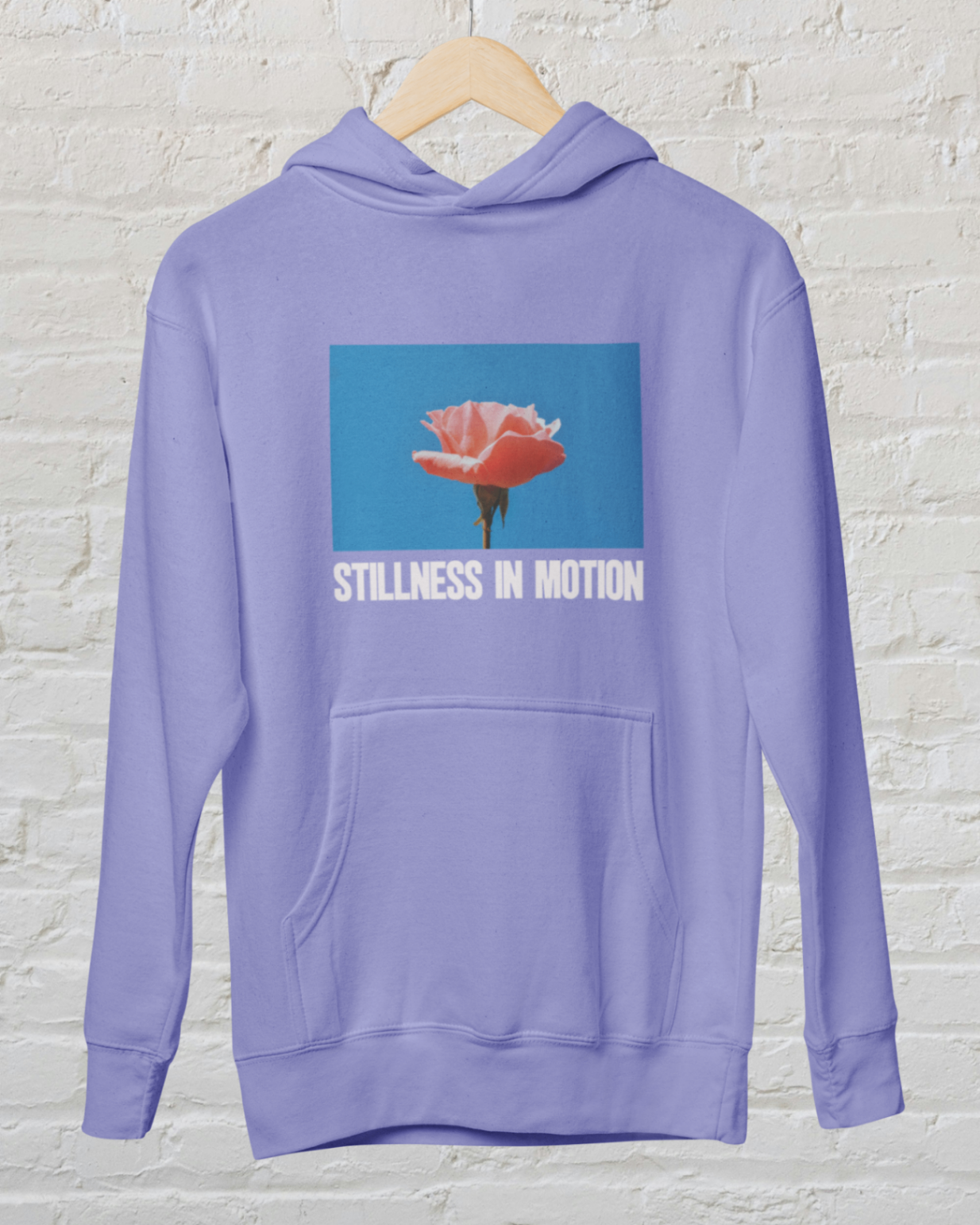 a violet hoodie with stillness in motion in text under a picture of a pink flower on blue sky backround