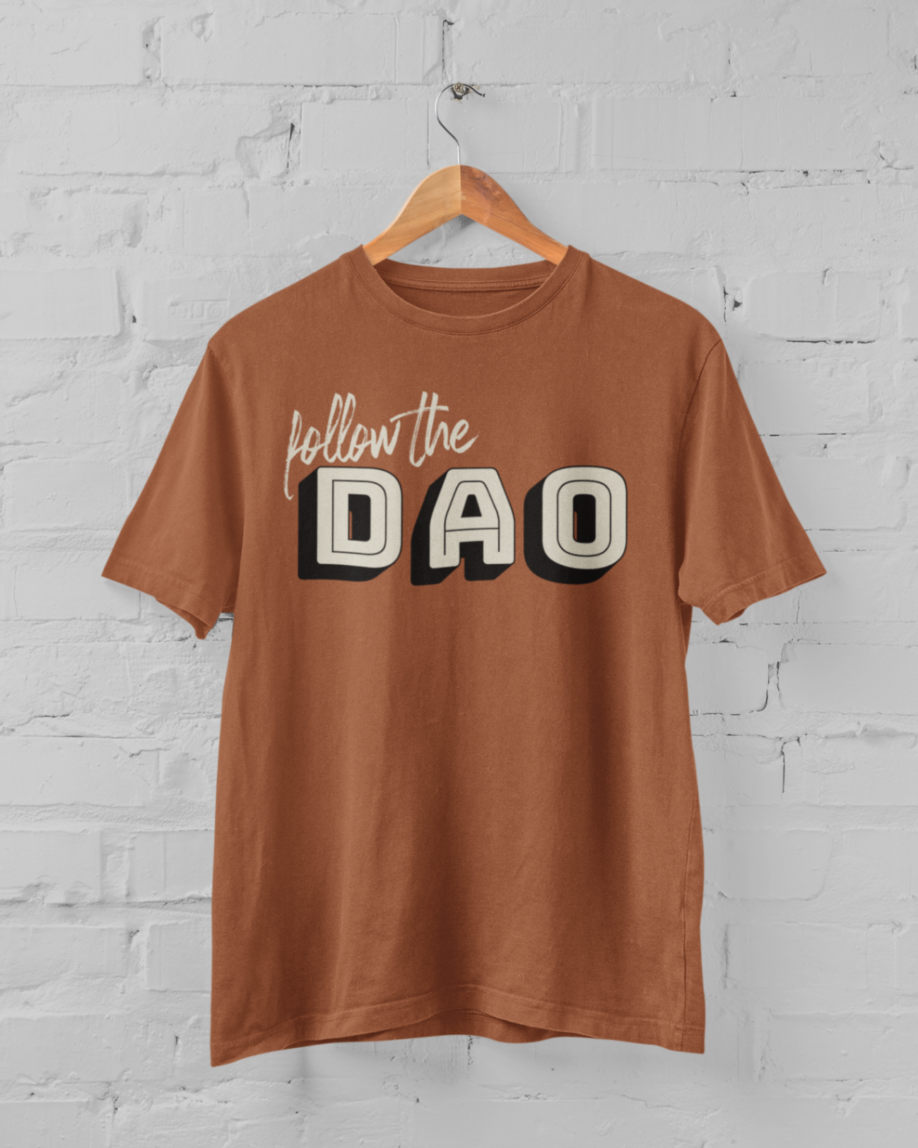 an autumn coloured t shirt with follow the dao design on a hangar in front of a white brick backround
