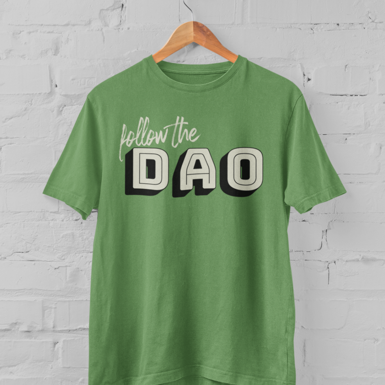 a leaf coloured t shirt with the follow the dao design on a hangar in front of a white brick backround
