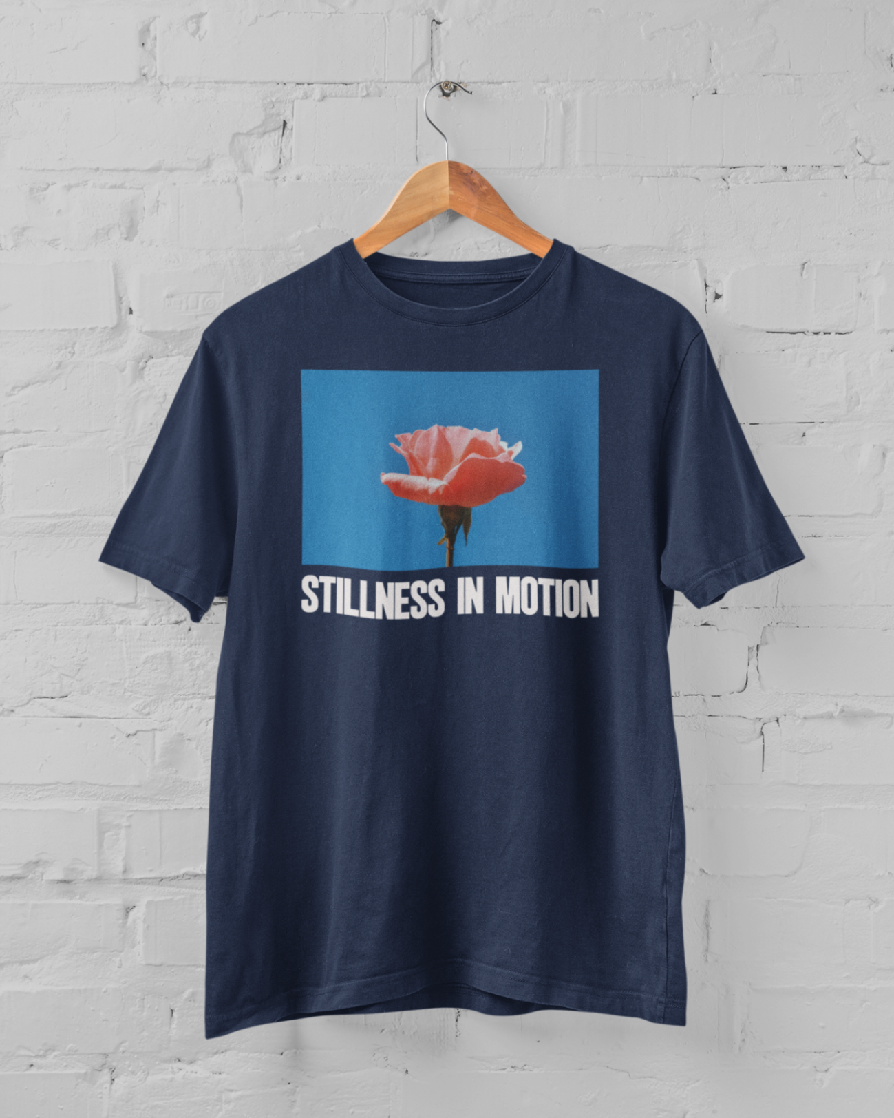 a navy tshirt with stillness in motion written in text under a pink flower over a sky blue backround