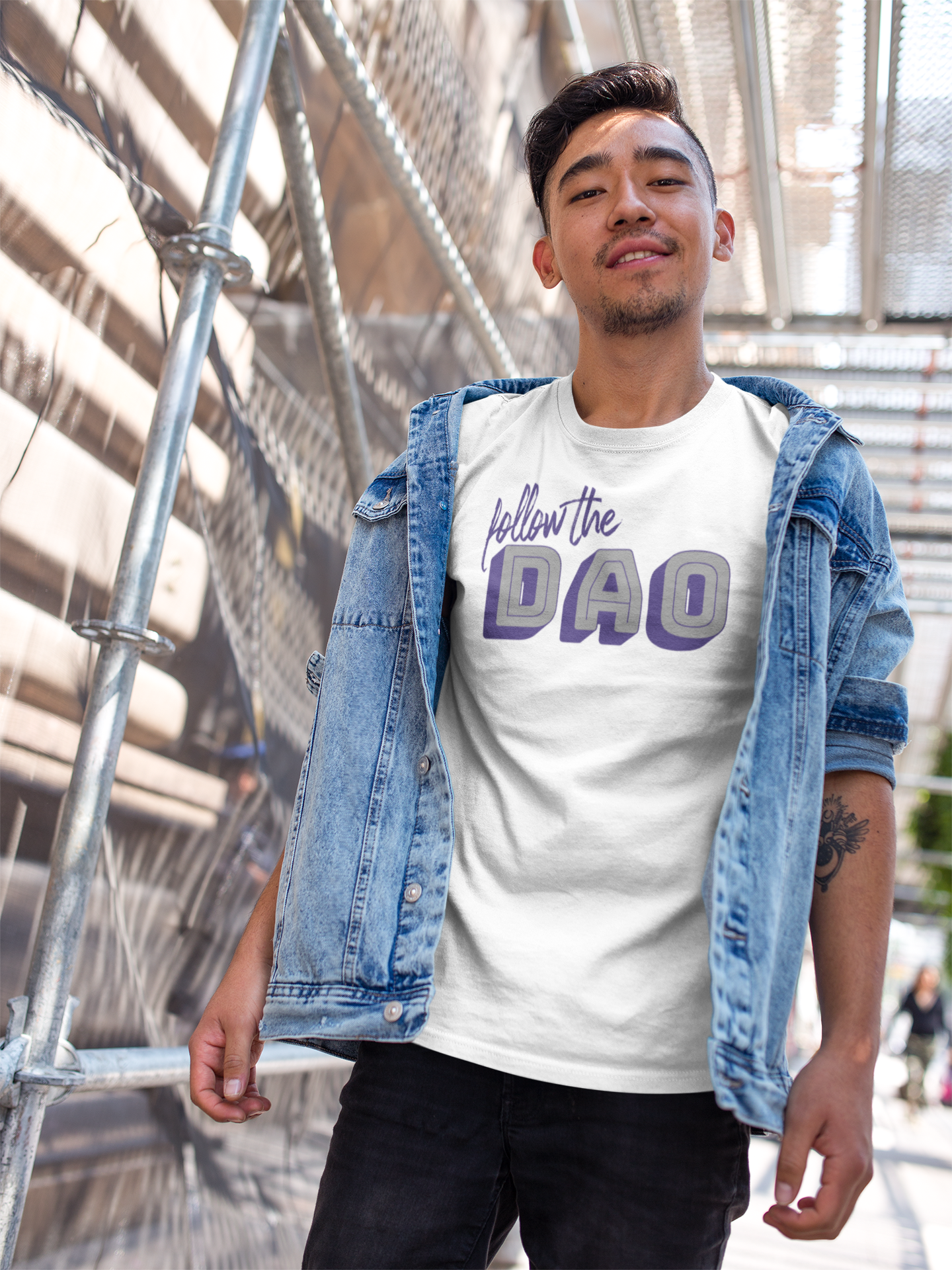 a cool asian man wearing white follow the dao t shirt with purple and grey lettering in an urban setting