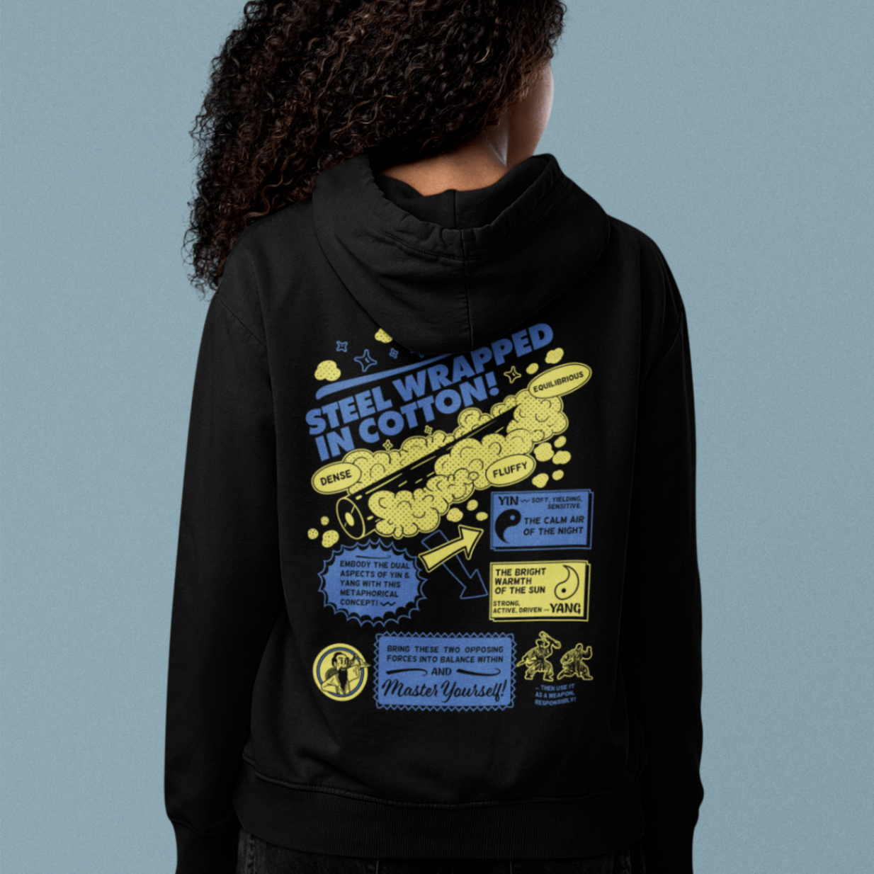 back view of a female model wearing a black zip up hoodie with steel wrapped in cotton design in yellow and navy text 