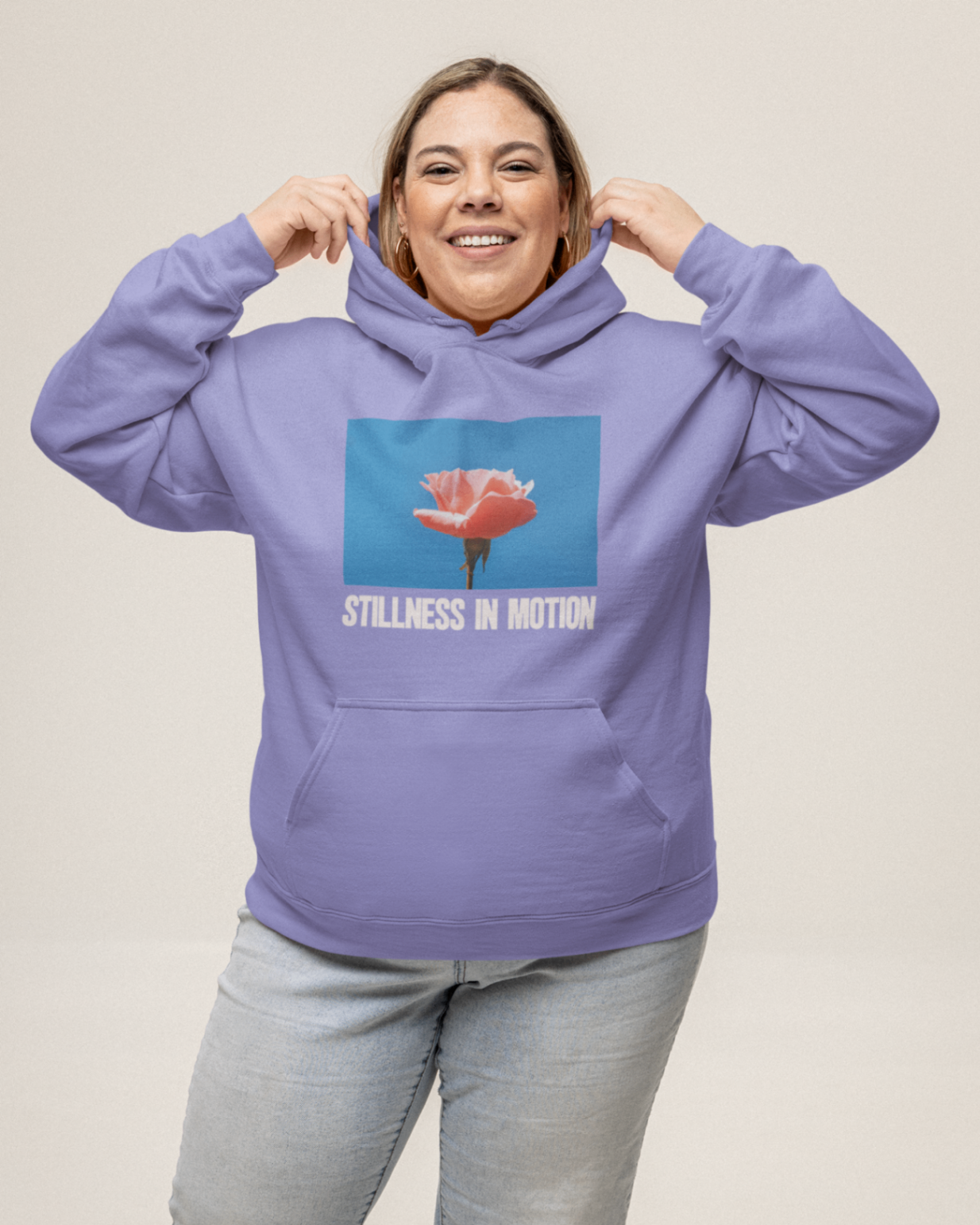 a woman wearing a violet hoodie with stillness in motion written in text under a picture of a pink flower over a sky blue backround