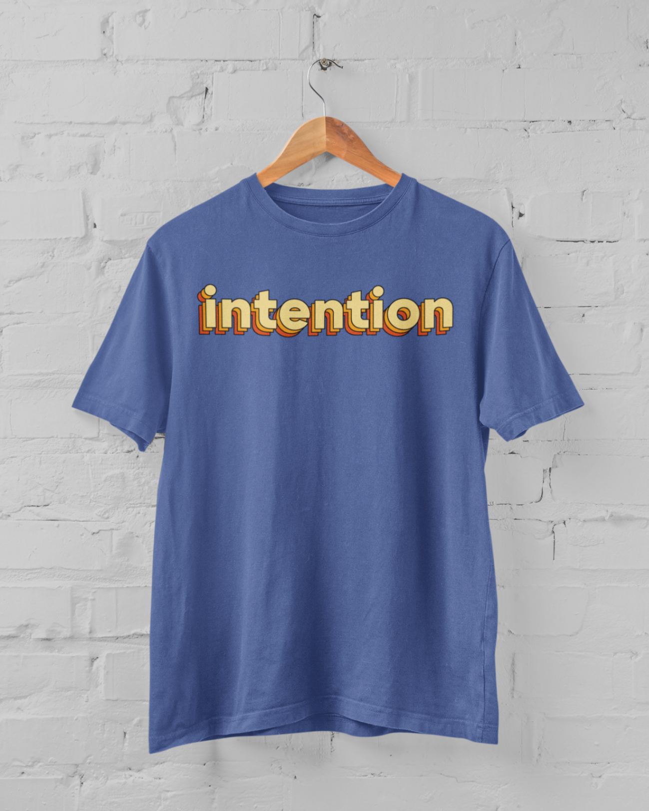 a royal blue t shirt with intention written in 3 D letters on a hanger in front of a white brick backround